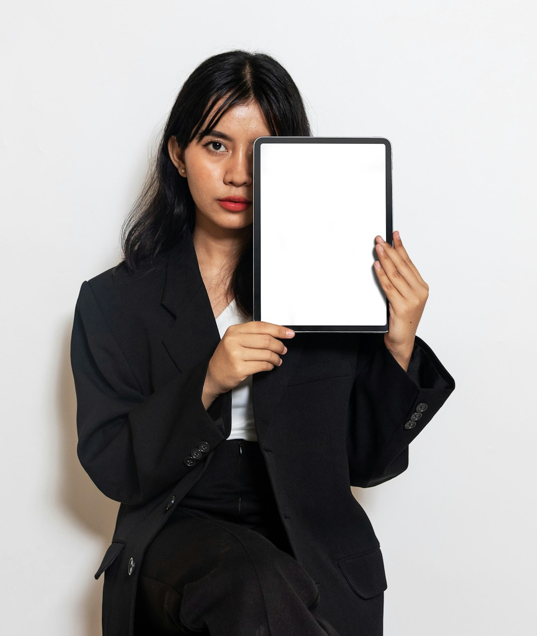 Woman holding an iPad and partially hiding her face behind it.
